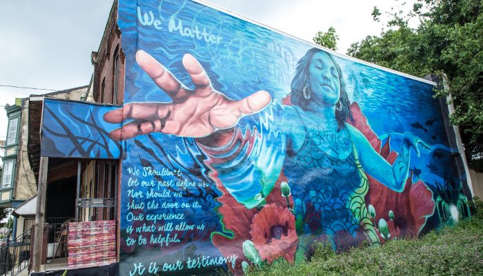 A mural in West Philly that shows a picture of a resilient woman reaching out, with the words, "We matter. We shouldn't let our past define us," as part of an inspirational poem.