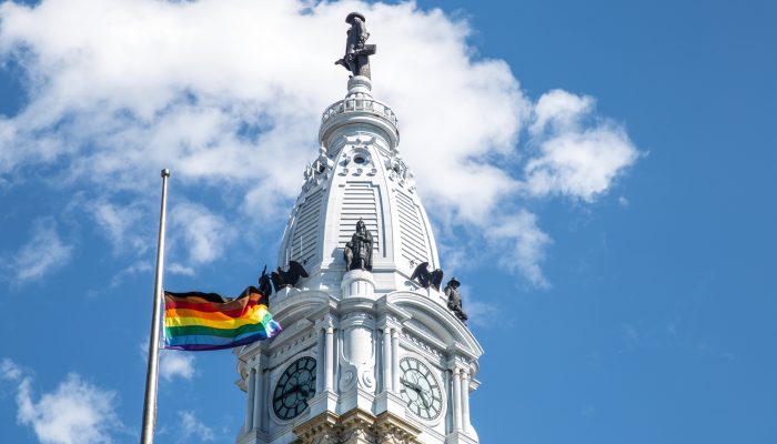 Rainbow striped flag flies in front of William Penn Statue at City Hall.