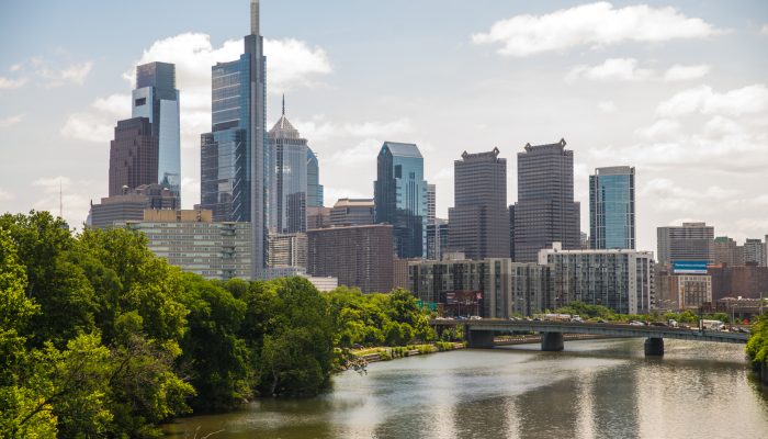 Philadelphia skyline with river and trees in the foreground.