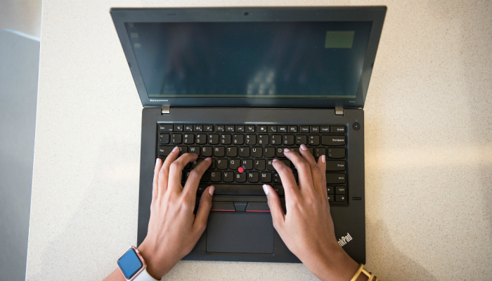 A women's hands type words on a laptop