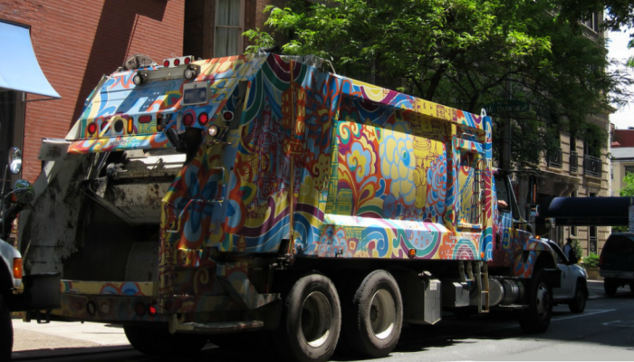 A City garbage truck decorated with artwork rolls through a Philadelphia street