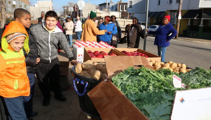 Student stand outside outside next to boxes of fresh fruits and vegetables