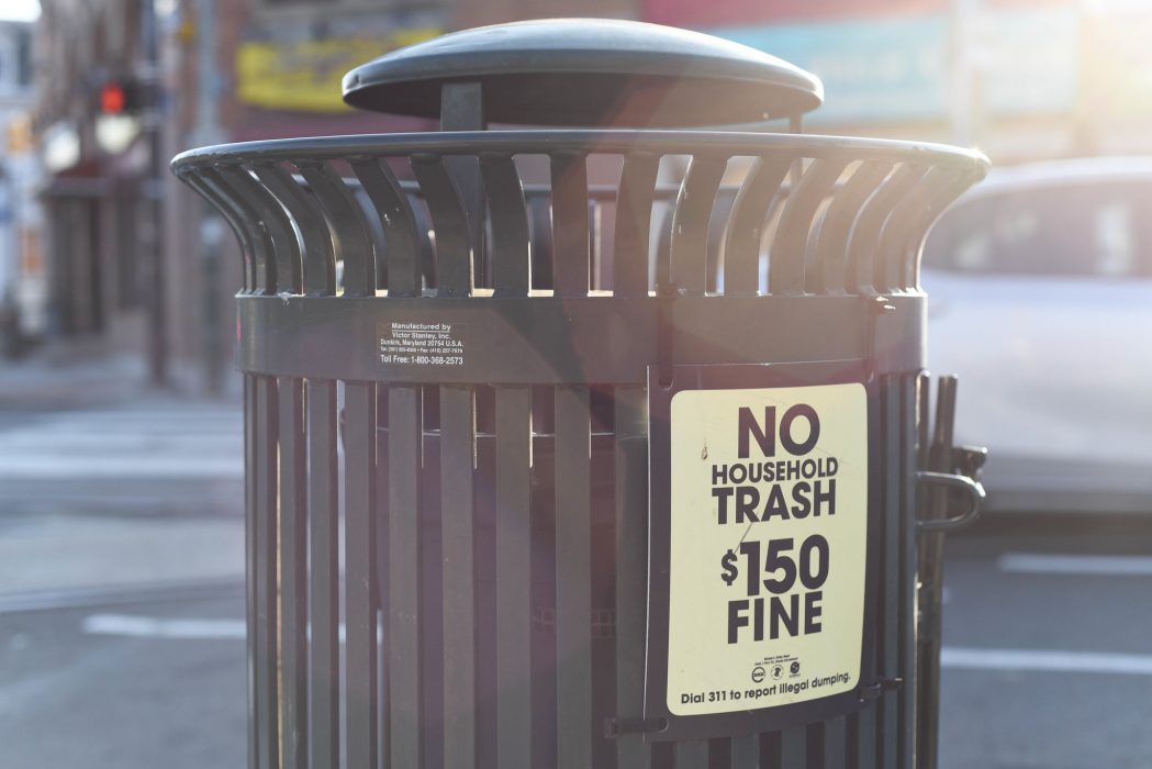 A public trash can with a sign reading no household trash $150 fine.