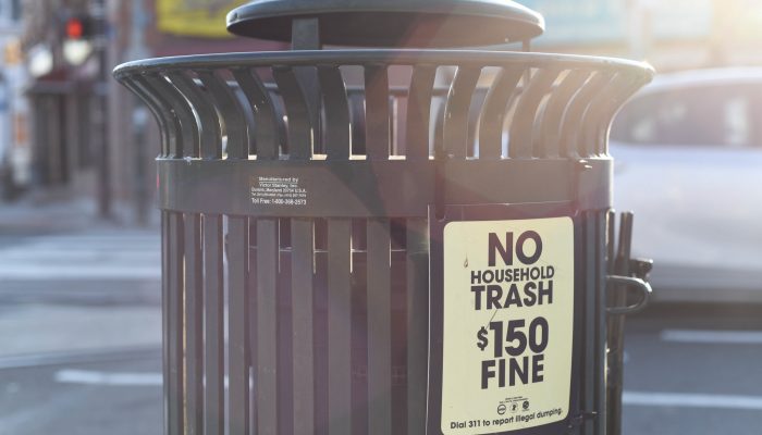 A public trash can with a sign reading no household trash $150 fine.