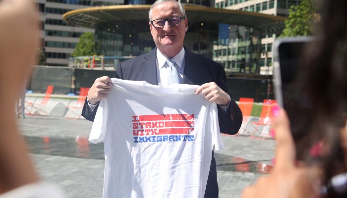 mayor kenney holding up a t-shirt that says I stand with immigrants