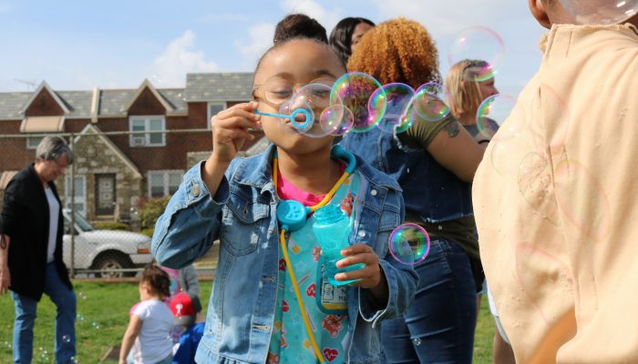 A PHLpreK student holding a bubble container and wand, blowing bubbles