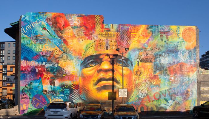 Mural depicting numerous people, featured on the side of a building.