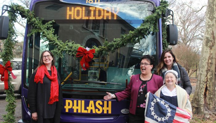 Commissioner Kathryn Ott Lovell poses with Betsy Ross and two other women in front of a bus decorated with garland and ribbons