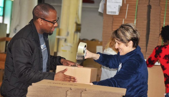 Two people taping up a cardboard box.