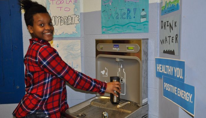 A student is smiling while filling up a water bottle at a school hydration station