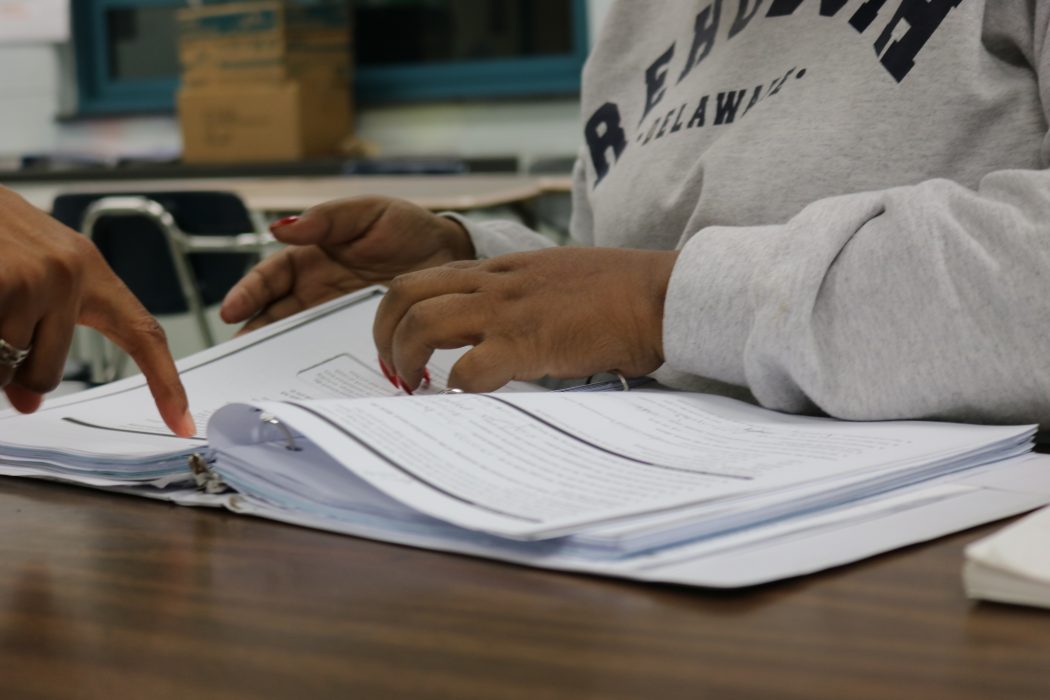 An adult education student's hands are on top of an open textbook, flipping through it.