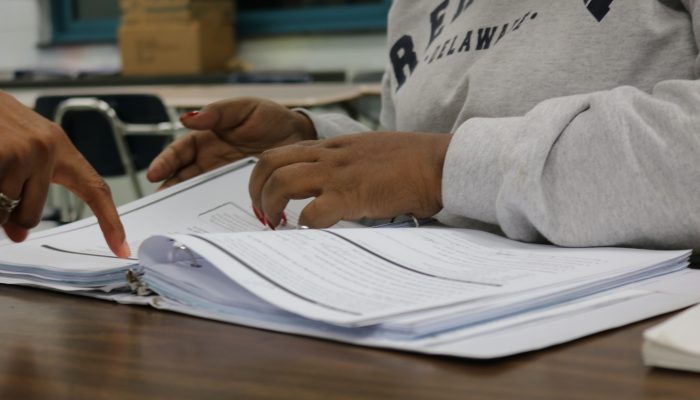 An adult education student's hands are on top of an open textbook, flipping through it.