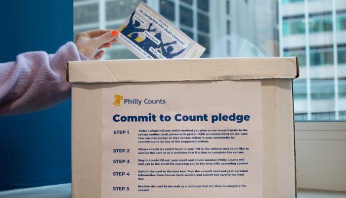 Person placing a completed Commit to Count card into a white collection box labelled "Commit to Count pledge".