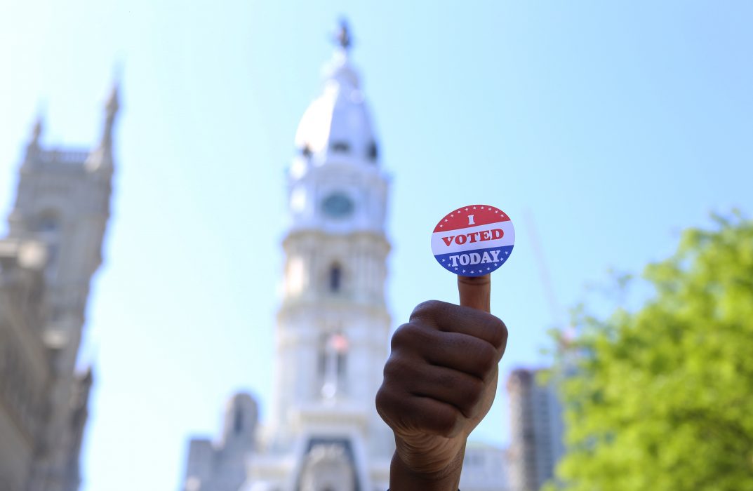 person holding up a voting sticker on their thumb
