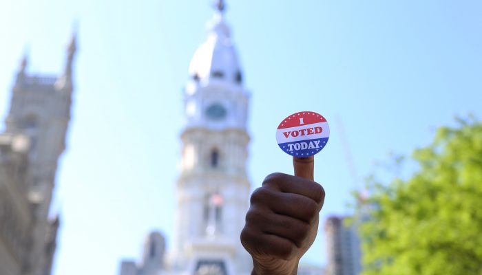 person holding up a voting sticker on their thumb