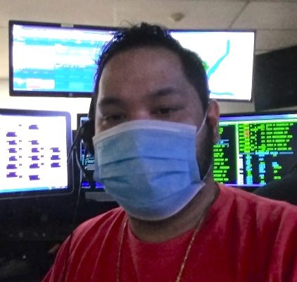 man in face mask with several computer screens behind him