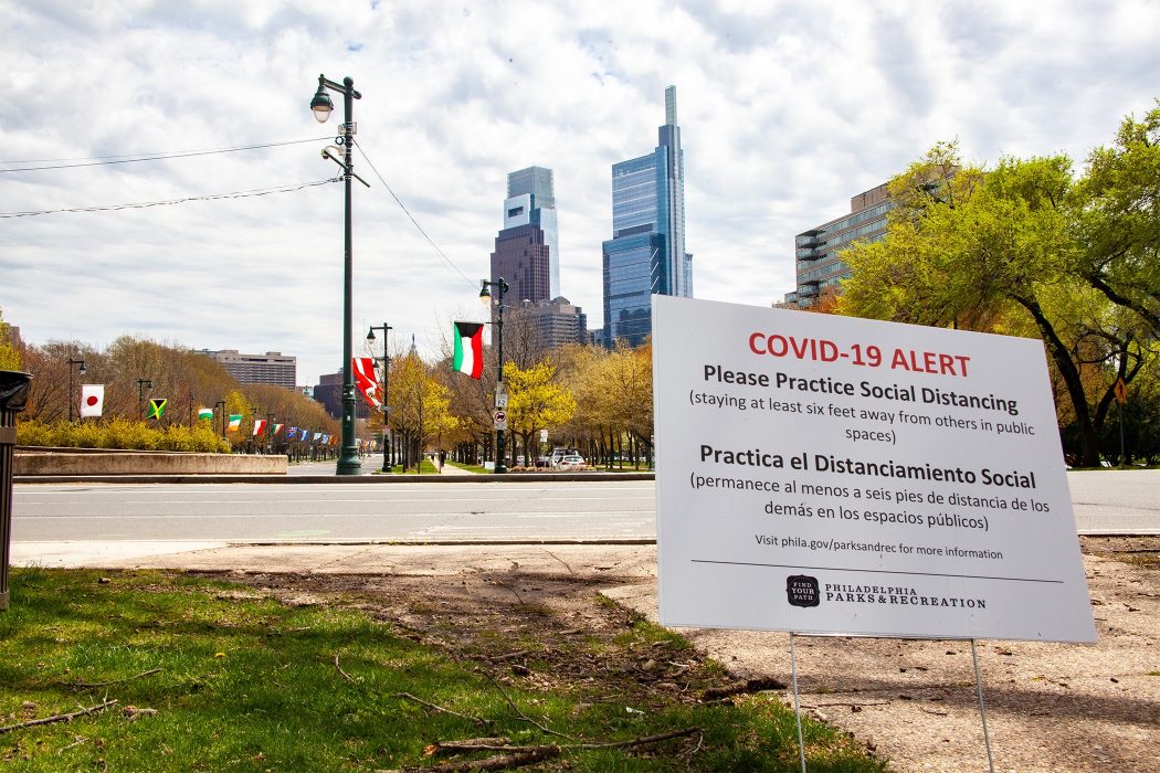 The Center City skyline in the background rests behind a large sign reminding Philadelphians about COVID-19 and social distancing.