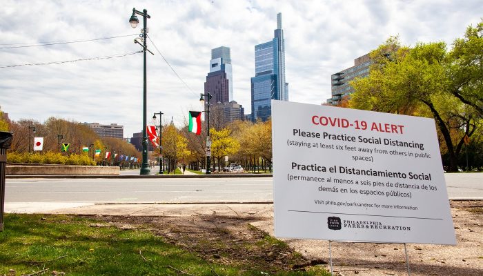 The Center City skyline in the background rests behind a large sign reminding Philadelphians about COVID-19 and social distancing.