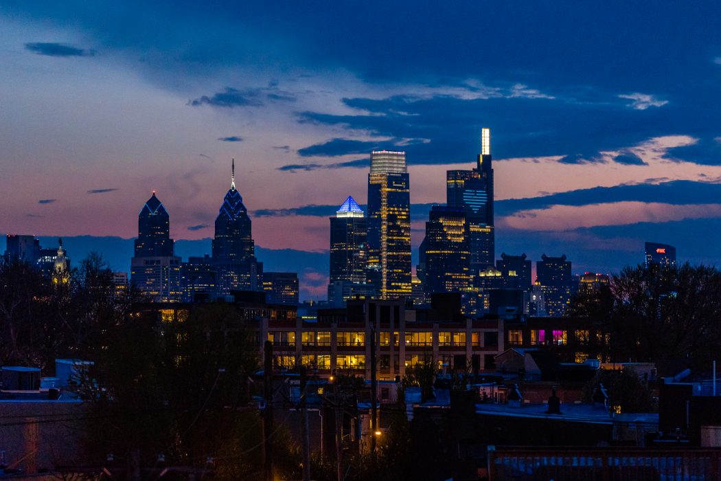 the philadelphia skyline at night lit up with blue lights to honor healthcare workers and essential workers during COVID-19