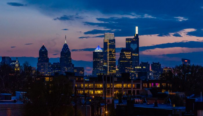 the philadelphia skyline at night lit up with blue lights to honor healthcare workers and essential workers during COVID-19