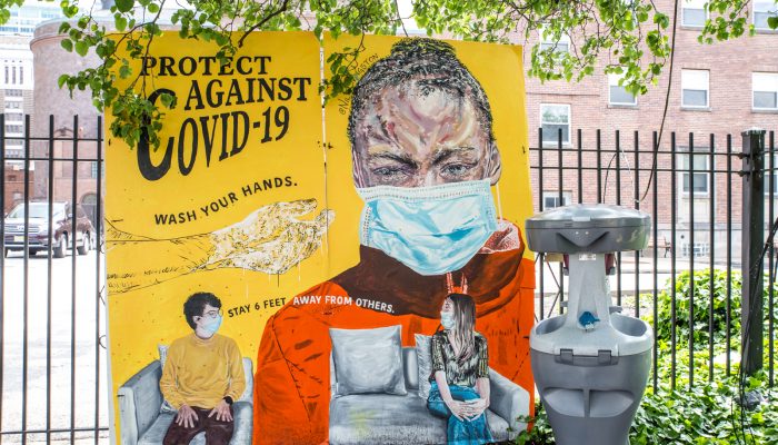 an outdoor handwashing station with a mural of a person wearing a mask that says protect against covid-19