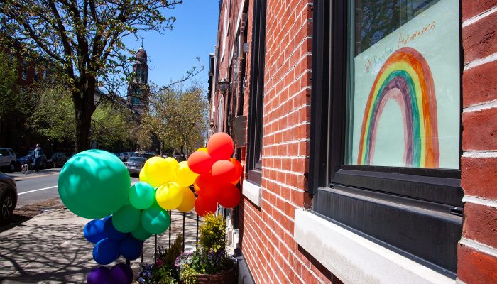 A sign hangs in a Philly row home window. It says # Rainbow Awesomeness. Balloons are outside of the home on the stairwell.
