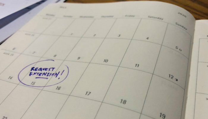 A calendar is marked with a reminder to request an extension on July 15