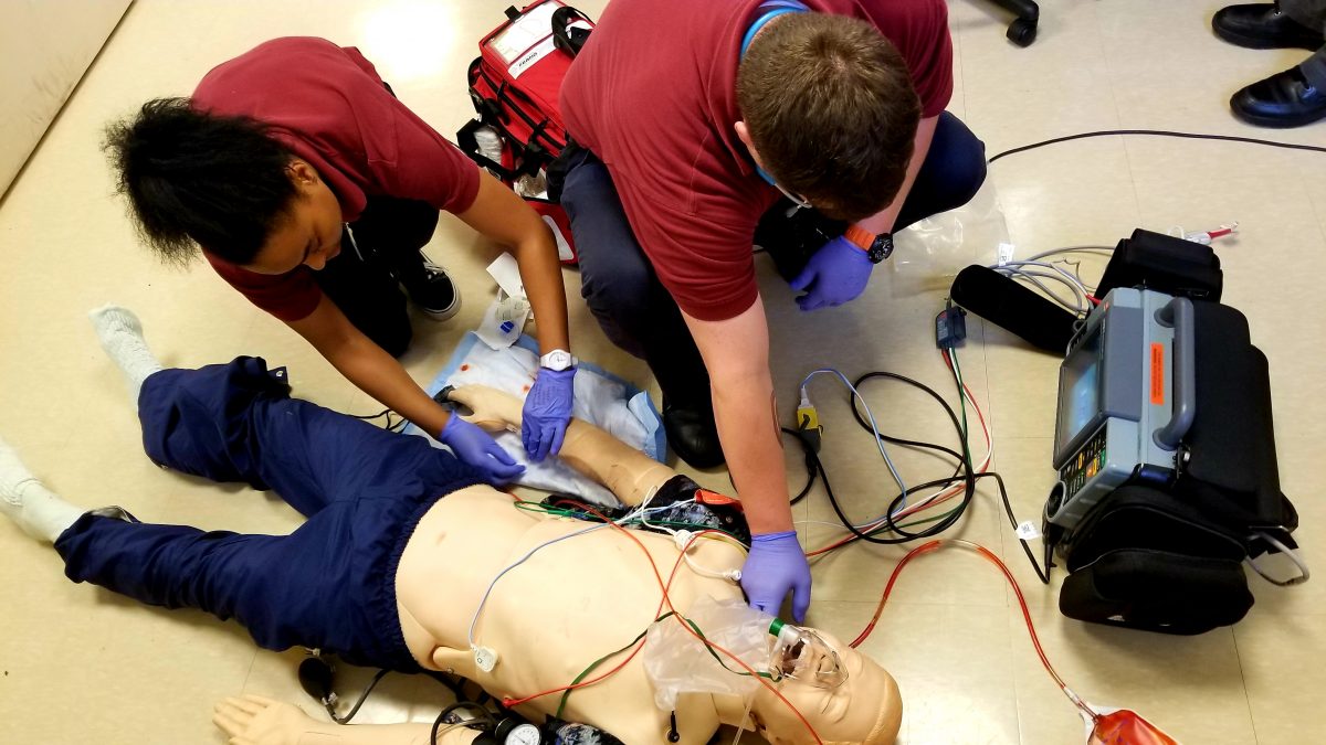 man and woman kneel over intubated dummy lying on floor