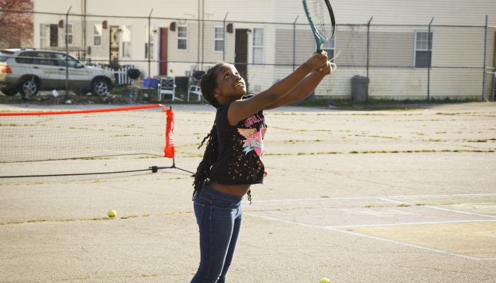 A student playing tennis, holds a tennis racket in a school playground.