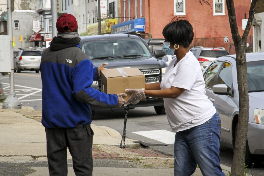 A woman wearing a mask and gloves hands a box of produce to a Philadelphia resident