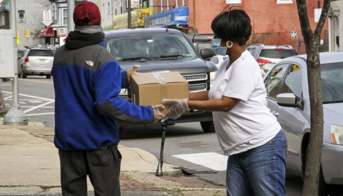 A woman wearing a mask and gloves hands a box of produce to a Philadelphia resident