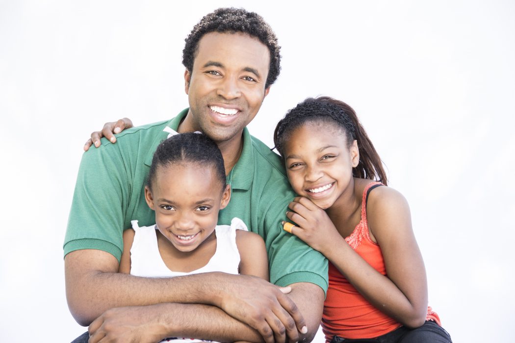 A father and his two daughters pose for the camera, smiling.