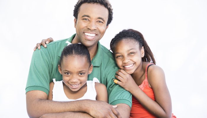 A father and his two daughters pose for the camera, smiling.