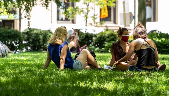 people wearing masks sitting in a small group on the grass in a park
