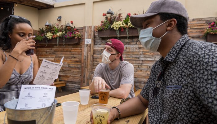 Three people eating at a table; two people are wearing masks.