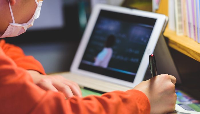 A student sits in front of a tablet, writing.