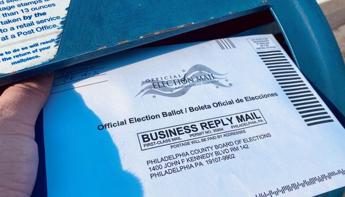 a person putting a mail-in ballot into a mailbox
