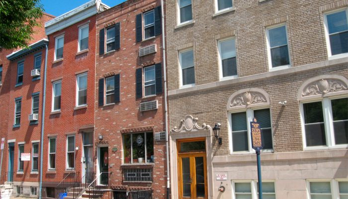 Several brick Philly rowhomes next to a much larger apartment building.