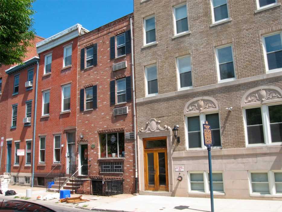 Several brick Philly rowhomes next to a much larger apartment building.