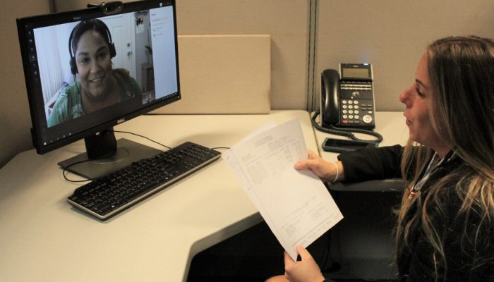 A woman sits in front of a computer monitor. On the monitor, a legal services representative from the Department of Revenue assists the customer via a video link.