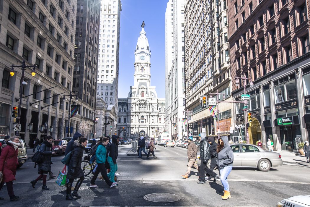 A group of people crossing Broad Street in front of Philadelphia City Hall.