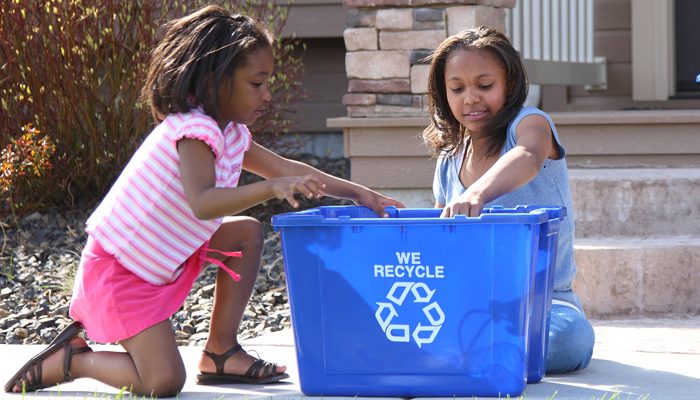 Duas meninas com um balde de reciclagem azul