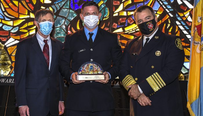 three men standing in front of stained glass window with one man holding replica of stained glass window