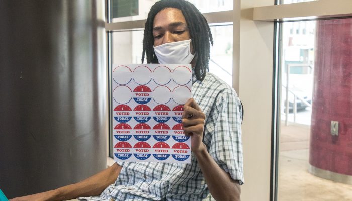 Man in mask holding a sheet of I Voted stickers