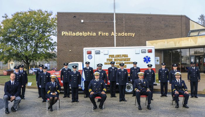 paramedics in dress uniforms stand in front of ambulance outside brick building that says Philadelphia Fire Academy