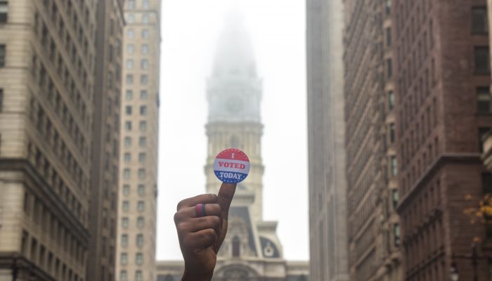 a person with an i voted sticker on their thumb in front of city hall on a foggy day