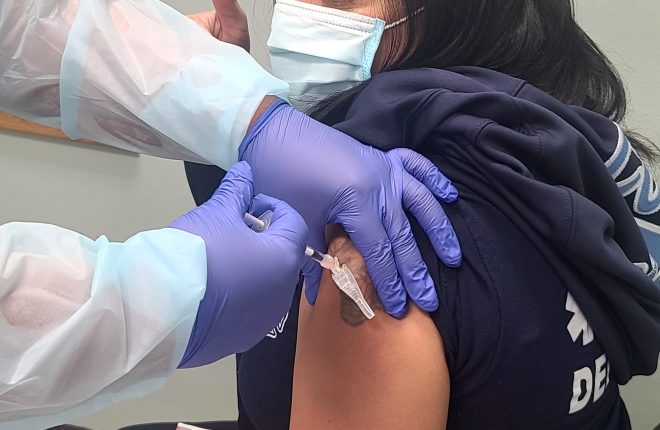 gloved hands plunging syringe into arm