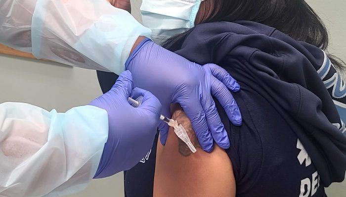 gloved hands plunging syringe into arm