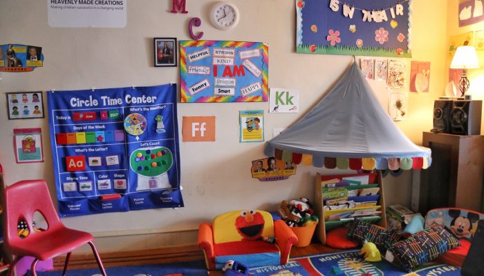 An empy classroom with a circle time poster on the wall, a child's couch on the flor and books
