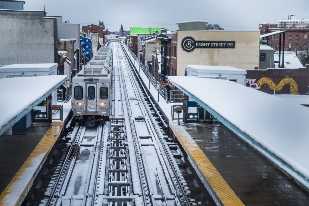 A subway train is departing from a snow-covered above ground platform.